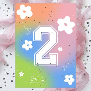 May include: A birthday card with a colorful gradient background of orange, pink, blue, and green. The number "2" is prominently displayed in white with a collegiate font. White flowers, hearts, stars, and a cloud graphic decorate the card. Silver star confetti and pink ribbon are in the background.