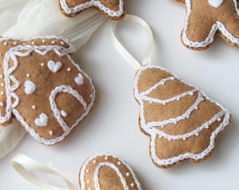 May include: Five felt Christmas ornaments in the shape of a star, gingerbread man, house, Christmas tree, and heart. Each ornament is decorated with white embroidery and white beads.