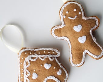 May include: Two felt gingerbread ornaments, one shaped like a gingerbread man and the other shaped like a gingerbread house. Both ornaments are decorated with white stitching and white beads.