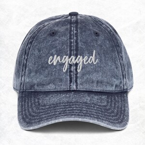 Puede incluir: Una gorra de béisbol de mezclilla azul con la palabra "engaged" bordada en blanco en la parte delantera.