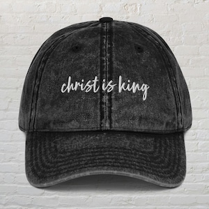 May include: Black distressed denim baseball cap with white embroidered text that reads "christ is king".