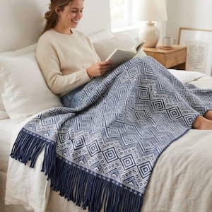 Puede incluir: Una manta rectangular con un patrón geométrico de diamantes en azul marino y blanco. La manta está terminada con flecos largos y gruesos de color azul marino a lo largo del borde inferior, aportando un borde texturizado al diseño.