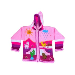 Puede incluir: Cárdigan rosa con capucha y cierre de cremallera. El suéter presenta diseños bordados coloridos de un sol, una llama, un cactus, una nube de lluvia, una casa y un pollo. Los puños y el forro de la capucha son de un rosa más oscuro. Tejido suave.