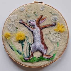 May include: A white and brown rabbit with a fluffy tail is jumping in a field of yellow dandelions and white puffballs. The rabbit is surrounded by green grass and white flowers. The scene is embroidered on a cream-colored fabric.