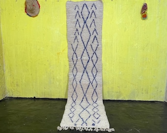 May include: A white and blue patterned rug with a diamond design. The rug is hanging on a yellow wall.