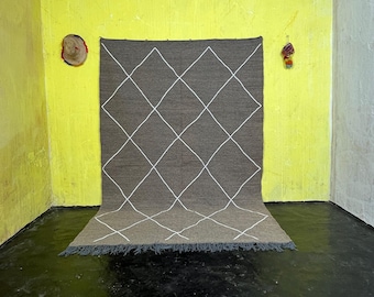 Puede incluir: Una alfombra marrón y blanca con estampado de rombos y borde de flecos. La alfombra está colocada sobre un suelo negro frente a una pared amarilla.