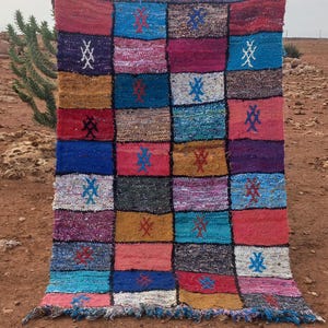 Könnte beinhalten: Ein bunter Patchwork-Teppich mit geometrischem Muster. Der Teppich ist aus gewebtem Stoff und hat einen Fransenrand.