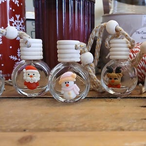 May include: A set of seven small, clear glass spherical bottles, each featuring a unique miniature Christmas-themed figurine inside, including a gift, Santa, snowman, reindeer, bell, tree, and stocking, topped with a ribbed wooden cap and twine.