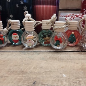 May include: Eight small round glass ornaments with a variety of Christmas-themed designs. The ornaments are hanging from a string and have a wooden top. The ornaments are on a wooden surface.