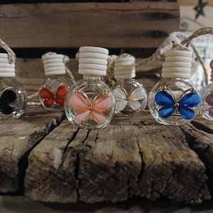 May include: Six glass bottles with butterfly charms hanging from a string. The bottles are clear and contain different colored butterflies. The butterflies are black, red, orange, white, blue, and purple.