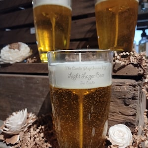 May include: Three glass beer-shaped gel candles. The candle in the foreground is labeled "The Candle Shop Geneva NY Light Lager Beer Gel Candle".