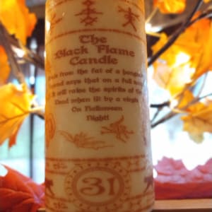 May include: A white candle with an orange label that reads "The Black Flame Candle". The label also includes text about the candle's origins and use. The candle has a large orange number "31" on the bottom.