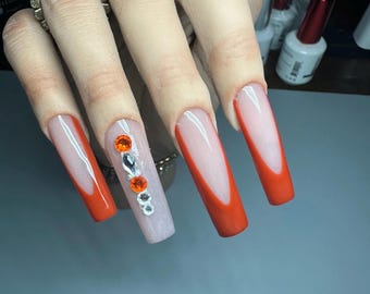 Longs ongles carrés coniques en acrylique avec pointe française orange brûlé et beaux strass de haute qualité.