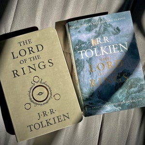 Pu&ograve; includere: Due copie de Il Signore degli Anelli di J.R.R. Tolkien. Un libro ha una copertina color sabbia con un simbolo dell'occhio in lamina d'oro e testo nero. L'altro &egrave; un'edizione del 50&deg; anniversario con copertina blu di montagna e scritte dorate.