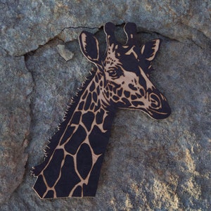 May include: A black and white wooden cutout of a giraffe's head. The giraffe's head is facing to the right and has a detailed pattern of spots.