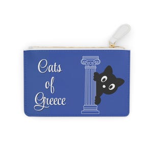 Puede incluir: Un estuche azul con el texto "Cats of Greece" en escritura blanca. Un gato negro se asoma por detrás de una ilustración blanca de una columna griega. El estuche tiene una lengüeta blanca y una cremallera dorada.
