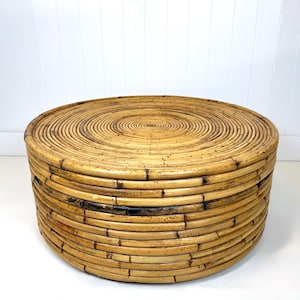 May include: A round, natural-toned rattan coffee table. The table is constructed from tightly woven, concentric circles of rattan, creating a textured surface. The design is a warm, neutral color, suitable for a living room or patio.