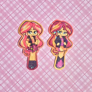 May include: Two cartoon stickers featuring a character with red and yellow hair, wearing a black jacket, purple skirt, and boots. The stickers have a yellow outline and are set against a pink plaid background.