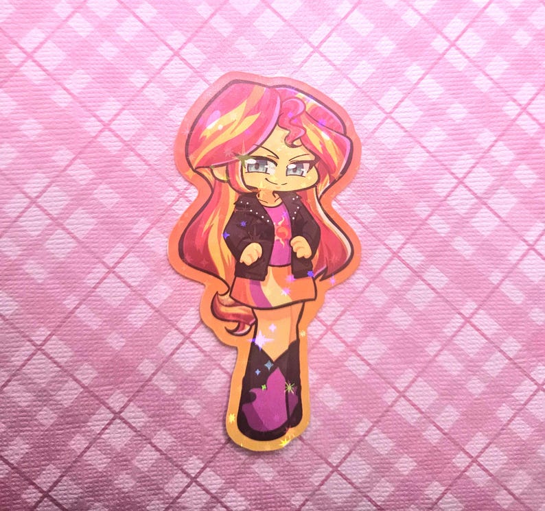 May include: A colorful sticker featuring a cartoon character with long, flowing hair in shades of yellow, orange, and pink. The character wears a black jacket, a pink shirt, and a skirt. The sticker has a glittery, holographic finish and is set against a pink background.