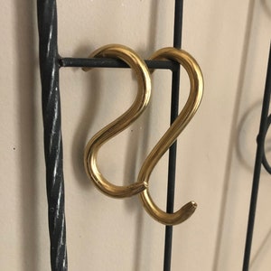 May include: Two gold-colored S-shaped hooks attached to a black metal frame.
