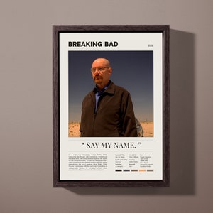 Peut inclure: Une affiche encadrée avec une image en noir et blanc de Walter White de la série télévisée "Breaking Bad". L'affiche porte le titre "Breaking Bad" et la citation "Say My Name." L'affiche est sur un mur beige.