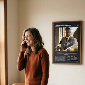 American Gangster poster, Dark edition, framed and on a wall beside someone laughing on the phone