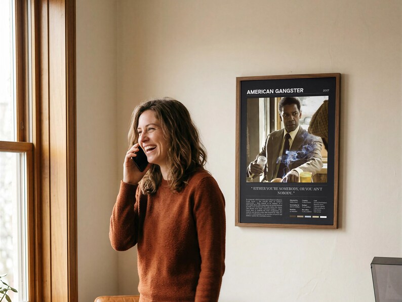 American Gangster poster, Dark edition, framed and on a wall beside someone laughing on the phone