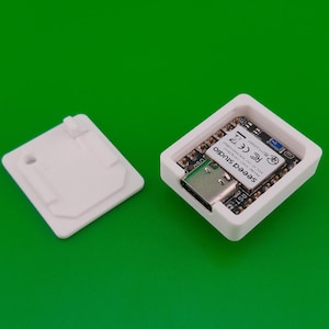 Könnte beinhalten: Ein weißes Plastikgehäuse mit einer kleinen Platine im Inneren. Die Platine hat einen USB-C-Anschluss und den Text "Seed Studio" darauf gedruckt. Das Gehäuse hat eine kleine weiße Plastikabdeckung, die oben angebracht werden kann.