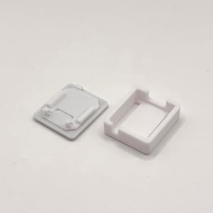 Puede incluir: Dos componentes de plástico blanco, uno rectangular con un interior empotrado y el otro una tapa a juego. La tapa tiene forma cuadrada con detalles en relieve y pequeñas protuberancias. Los artículos están sobre un fondo blanco.