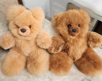 Può includere: Due orsacchiotti di peluche, uno marrone chiaro e uno marrone scuro, sono seduti su una superficie grigio chiaro. Entrambi gli orsi hanno occhi e nasi neri.