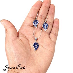 May include: A silver necklace and earrings set featuring a blue lapis lazuli leaf pendant and matching earrings. The jewelry is displayed on a hand.