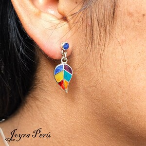 May include: Silver earrings with a colorful leaf design and a small blue gemstone. The leaf is made of different colored stones, including red, orange, yellow, green, and blue.