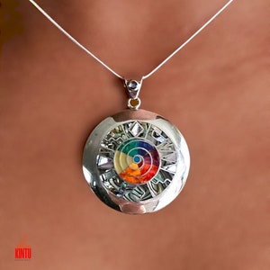 Puede incluir: Un collar de plata con un colgante redondo que presenta un dise&ntilde;o en espiral de colores rodeado de intrincados detalles de plata. El colgante est&aacute; hecho de n&aacute;car y otras piedras de colores.