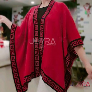 May include: A red knitted poncho with black and red geometric trim. The poncho has a loose fit and is open in the front. The text "JOYRA PERUVIAN" is visible on the poncho.