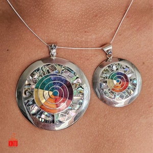 Puede incluir: Dos collares de plata con colgantes circulares que presentan un dise&ntilde;o de c&iacute;rculo conc&eacute;ntrico colorido hecho de n&aacute;car incrustado. El colgante m&aacute;s grande tiene un di&aacute;metro de unos 5 cm.