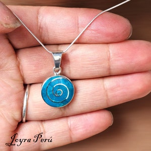 May include: A silver chain necklace with a turquoise blue pendant featuring a spiral design. The pendant is round and has a silver border.