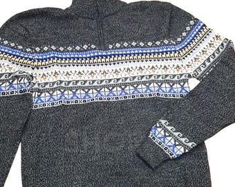 Può includere: Un maglione grigio scuro con zip e un motivo a fantasia blu, bianco e marrone. Il maglione presenta un collo alto e polsini a coste. Il motivo comprende forme geometriche e figure stilizzate.