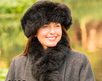 Può includere: Una donna indossa un cappello di pelliccia nero e una sciarpa abbinata. Il cappello è di stile a tesa larga con una corona arrotondata. La sciarpa è lunga e si avvolge intorno al collo.