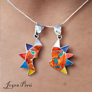 May include: A silver necklace with two pendants featuring colorful, geometric sun designs. The pendants are made of silver and enamel, and they are both in the shape of a sun with a face. The sun designs are in shades of red, orange, yellow, blue, green, and black.