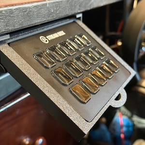 Peut inclure: Un Stream Deck avec plusieurs boutons rectangulaires transparents. L'appareil est noir avec un bord argenté et le logo Stream Deck. Les boutons sont disposés en grille.