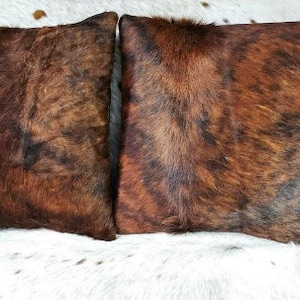May include: Two brown and black cowhide throw pillows with a soft, fuzzy texture.
