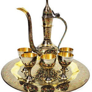 Puede incluir: Un juego de servicio de metal dorado con una jarra decorativa y seis tazas a juego. El juego está en una bandeja redonda con intrincados diseños florales.