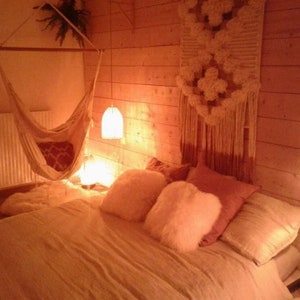 Puede incluir: Un dormitorio acogedor con una hamaca colgante, una cama con almohadas mullidas y un tapiz de macram&eacute; en la pared. La habitaci&oacute;n est&aacute; iluminada con una luz c&aacute;lida y ambiental.