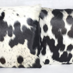 May include: Two black and white cowhide throw pillows with a soft, fuzzy texture.