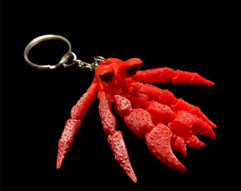 May include: A red plastic crab keyring with a silver key ring. The crab has detailed claws and a textured surface.