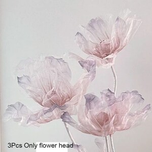 Puede incluir: Tres delicadas cabezas de flores transparentes en tonos rosa y morado. Las flores est&aacute;n hechas de un material ligero y transl&uacute;cido, lo que les da un aspecto suave y et&eacute;reo.