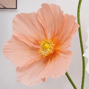 Peut inclure: Une grande fleur en papier p&ecirc;che avec un centre jaune et une tige verte. Les p&eacute;tales de la fleur sont textur&eacute;s et froiss&eacute;s, cr&eacute;ant une apparence r&eacute;aliste. La fleur est un objet d&eacute;coratif, probablement pour la d&eacute;coration int&eacute;rieure.