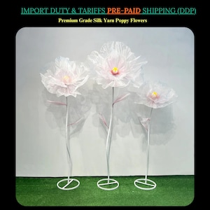 May include: Three artificial poppy flowers with white petals and yellow centres. The flowers are made of silk yarn and have long, silver stems. The text "Premium Grade Silk Yarn Poppy Flowers" is visible.