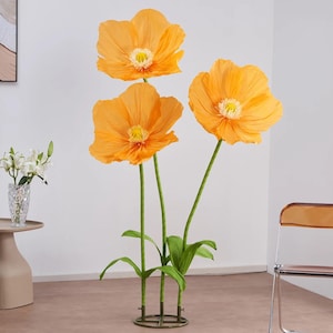 Peut inclure: Trois grandes fleurs de pavot artificielles orange avec des centres jaunes et des tiges vertes. Les fleurs sont dispos&eacute;es dans une base m&eacute;tallique d&eacute;corative, avec des feuilles vertes. Un accent vibrant pour la d&eacute;coration int&eacute;rieure.