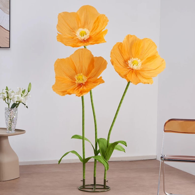 Peut inclure: Trois grandes fleurs de pavot artificielles orange avec des centres jaunes et des tiges vertes. Les fleurs sont dispos&eacute;es dans une base m&eacute;tallique d&eacute;corative, avec des feuilles vertes. Un accent vibrant pour la d&eacute;coration int&eacute;rieure.
